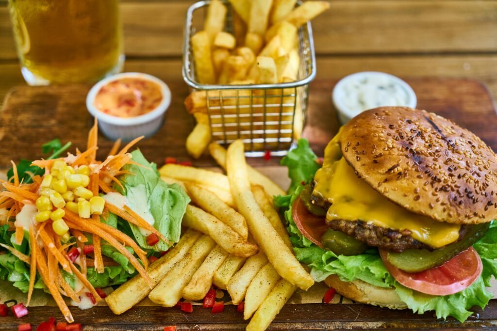 Delicious gourmet cheeseburger with crispy french fries and fresh salad on a wooden board.